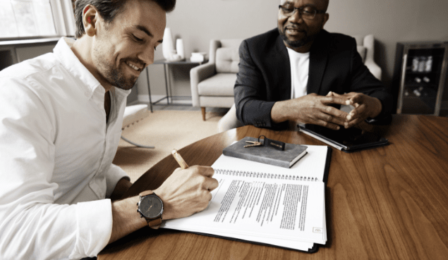 Two men sitting at a table in a Century 21 office reviewing and signing paperwork