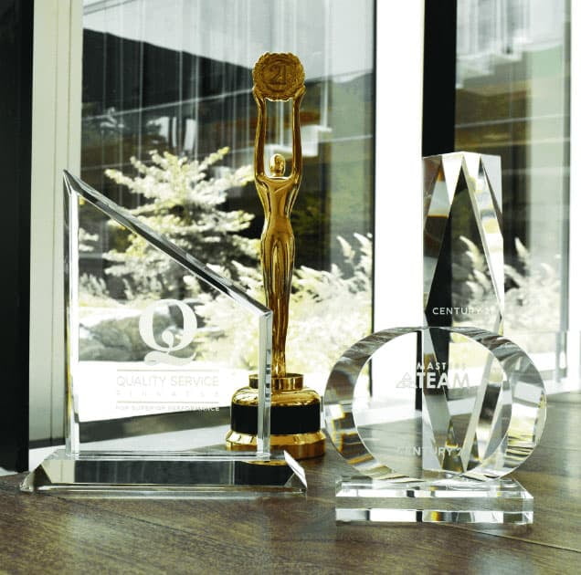 Four Century 21 award trophies arranged on a table in front of an office window